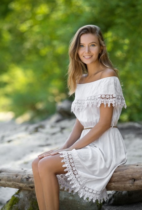 Pretty teen Clover removes an off shoulder dress to pose nude on driftwood