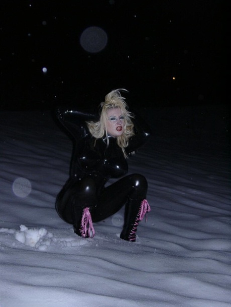 Pale blonde Avengelique models black latex clothing on snow-covered ground