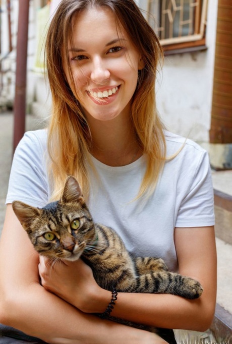 Tiener solo meisje Giselle houdt een kat vast voordat ze helemaal naakt gaat