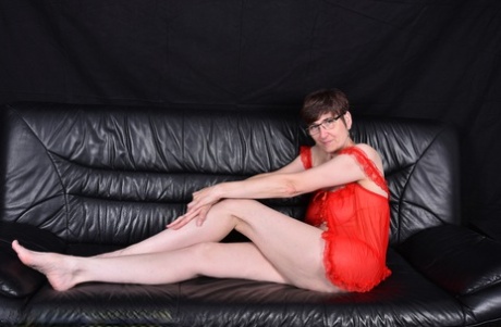 Mature brunette gets totally naked on a sofa while wearing glasses