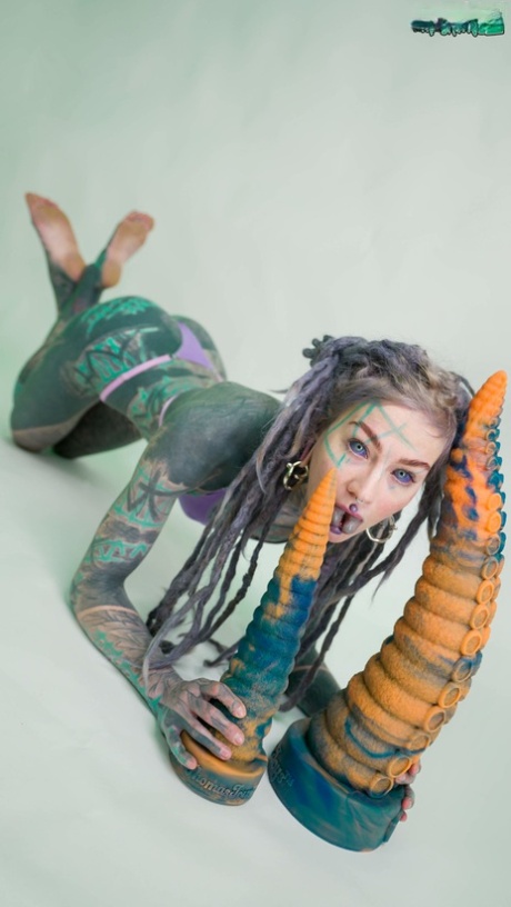 Una ragazza pesantemente tatuata, Anuskatzz, tiene in mano un paio di giocattoli taintacle nudi