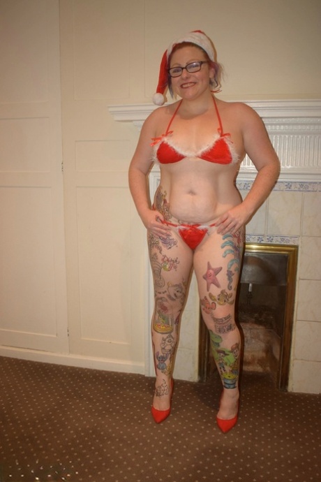 Une femme âgée tatouée se débarrasse d’une pose de bikini nue dans un bonnet de Père Noël