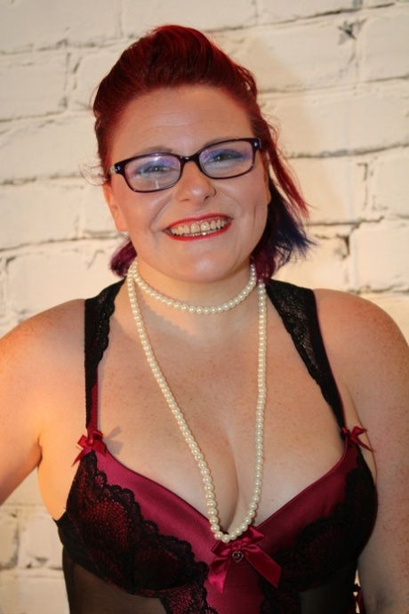 Buttet rødhåret kvinde løsner sine bryster fra lingeriet iført briller og nylonstrømper