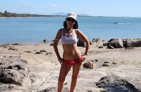 A MILF morena Roxeanne fica nua de óculos de sol na praia