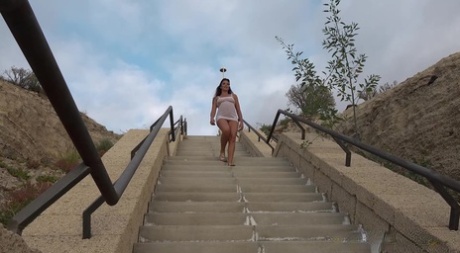 Den pene brunetten Sexy Lexy tisser på en offentlig trapp.