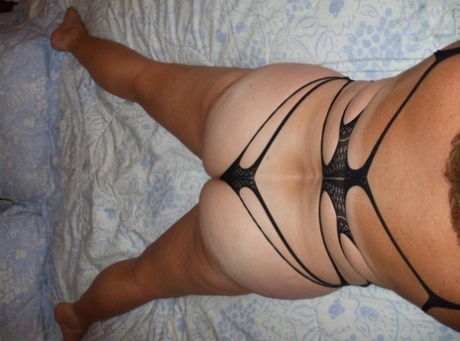 Äldre dam Busty Bliss poserar i avslöjande underkläder på en säng