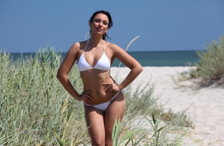 Lusse dans son bikini blanc joue avec le sable en ensoleillant son corps randonnant et ses jambes.