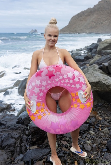 Charmantes blondes Teenie Decima wird nackt auf einem Innertube am Meer