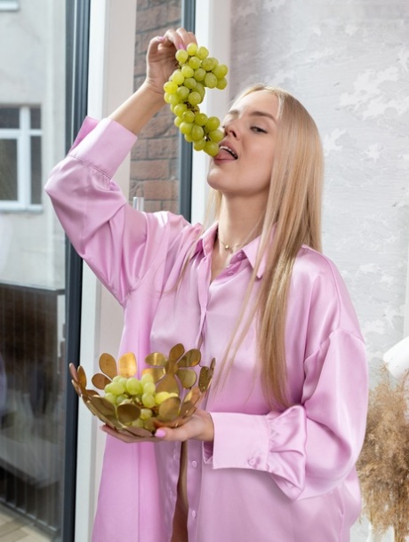 Słodka blond nastolatka Decima trzyma kiść winogron podczas całkowitego rozebrania się