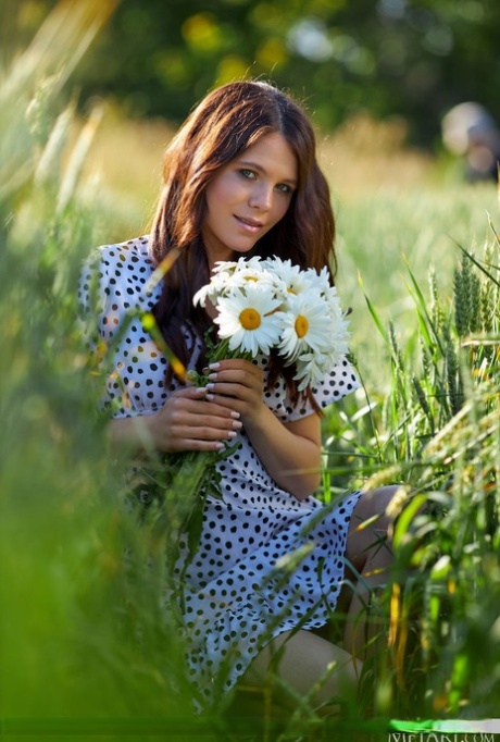 Mooie tiener Elena Max plukt wat wilde bloemen terwijl ze naakt in lang gras loopt