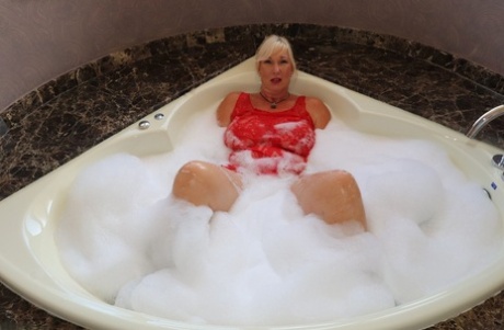 Older blonde fatty Melody partially removes a dress while taking a bubble bath