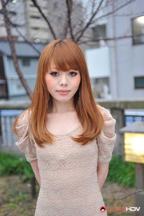 A japonesa Reika Kitahara, uma rapariga sexy de cabelo ruivo, posa ao ar livre com um vestido curto
