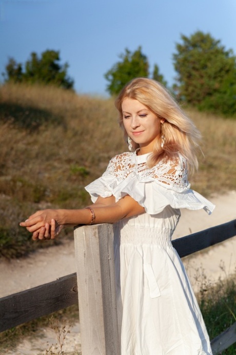 Zoete blonde tiener Claire verwijdert haar jurk om naakt te gaan tegen een landelijk hek