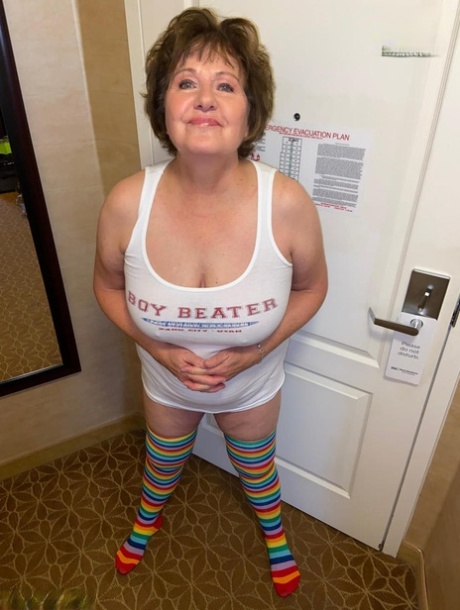 Mature lady Busty Bliss gets naked while wearing thigh-high rainbow socks