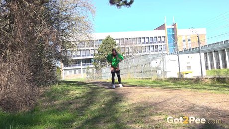 Pretty girl Naomi Benet takes a badly needed pee on a path near a fence