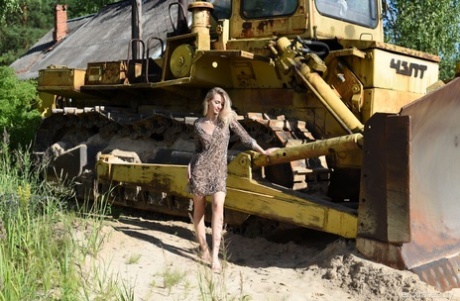 Blonde teen Ava List models naked upon heavy equipment during the day