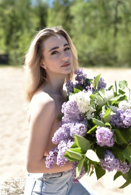 Thin blonde teen Leticia gets naked on sandy ground while holding flowers