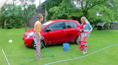 Unga tjejer blöter ner varandra på en bakgård medan de tvättar en kompakt bil