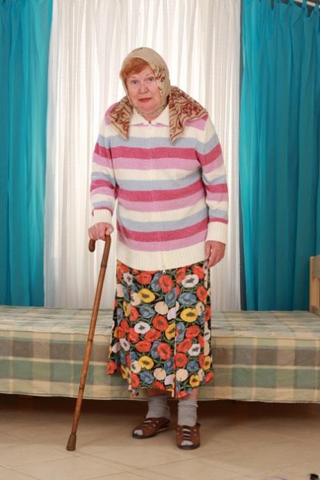 Stará tlustá babička Alice s holí pózuje plně oblečená v dlouhé sukni a ponožkách