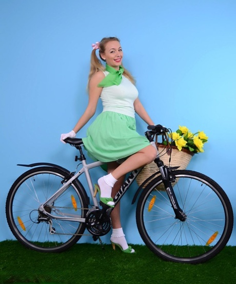 Söt blondin visar sina fasta bröst på en cykel i vita handskar och fransiga trosor