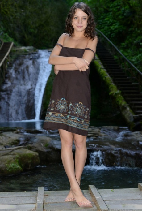 Süßes Teenie Nensi B modelliert nackt auf Holzbrücke vor Wasserfall