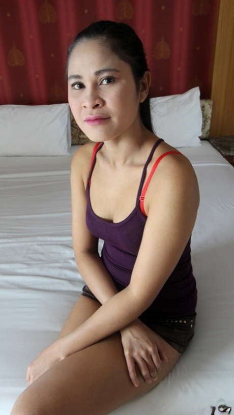 Ragazza thailandese sola si spoglia esitante su un letto per un turista sessuale
