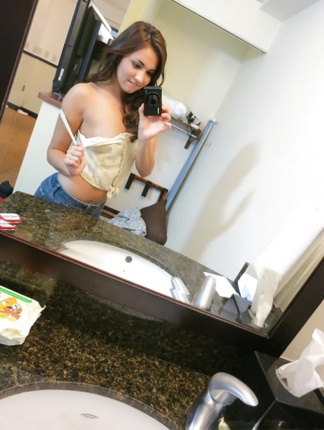 Pittige brunette stript voor de spiegel en maakt selfies