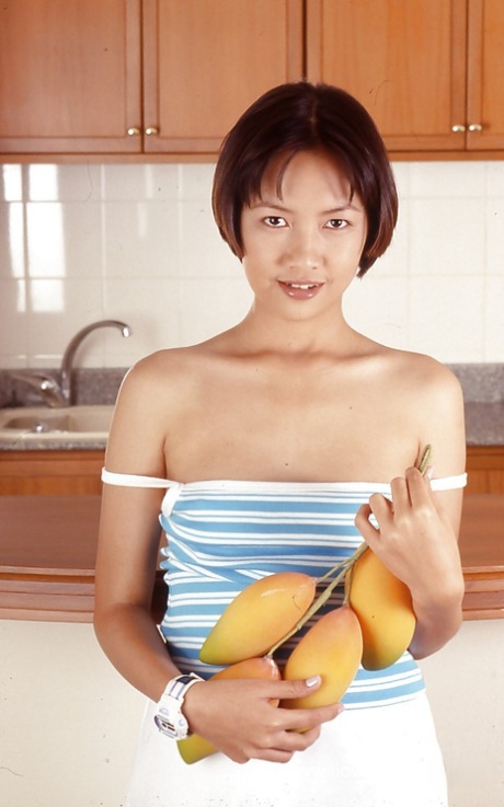 Asiática vestida com mamas pequenas posa na cozinha de pernas abertas