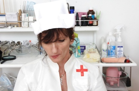 Oudere verpleegster Andula poseert in uniform voordat ze naakt stript en masturbeert