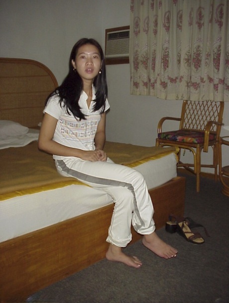 Ondeugende Aziatische babe die haar kleren uittrekt en op het bed poseert