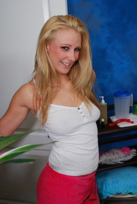 Smiley teenage blonde in pink shorts getting naked in the massage parlor