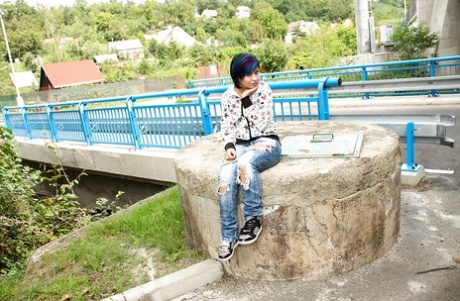 Adolescente fringante en blue-jeans se déshabillant et jouant avec ses trous rasés en plein air.