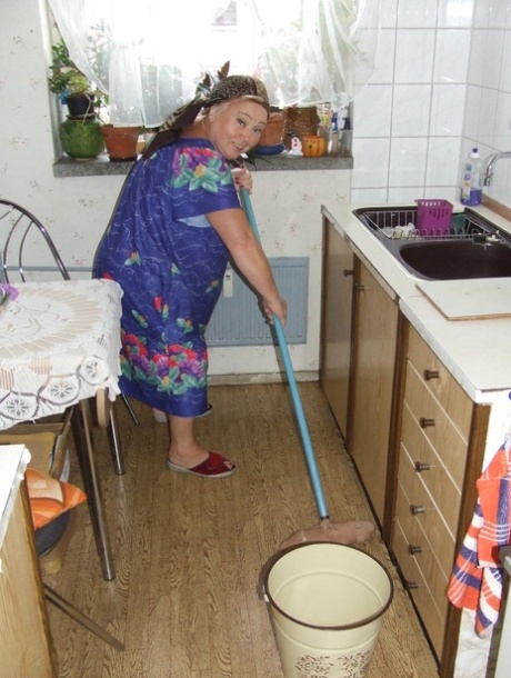 Dikke oma Regina kleedt zich uit en poseert terwijl ze de keuken schoonmaakt