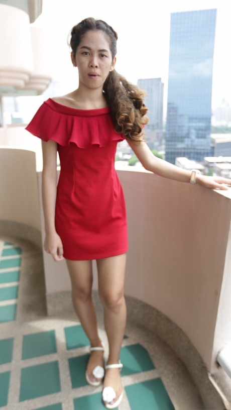 Söt nybörjare från Thailand poserar i sin röda klänning före modelljobbet