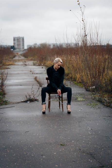 Shackled blonde bitch Ferggy spreads legs sitting on chair on rainy day