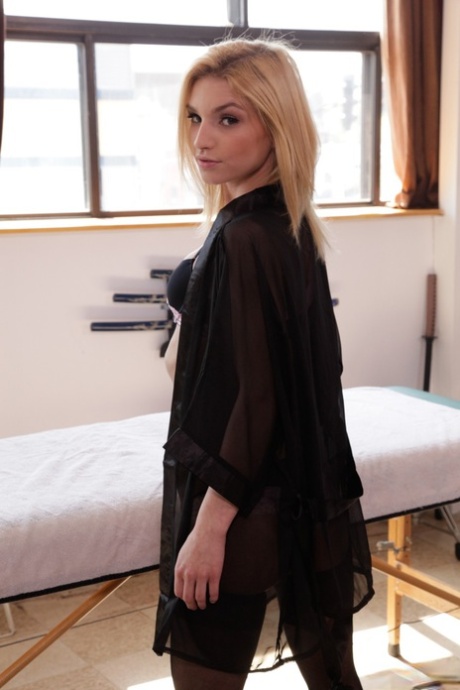 Smal blond tonåring Nikita Teen ser söt ut i en svart klänning och sexiga underkläder