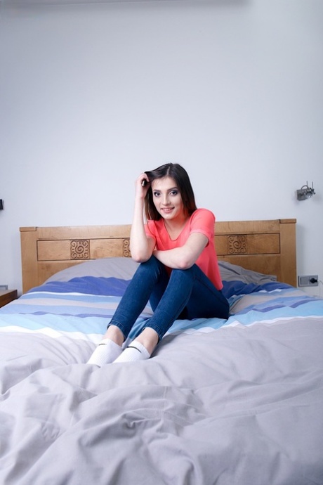 Fröhliche Teenagerin Maryln zieht enge Jeans und transparentes Shirt auf dem Bett aus