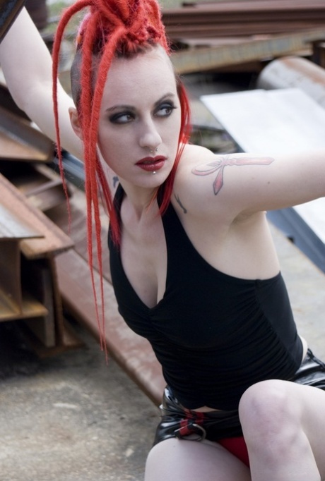 Punk-Mädchen mit roten Haaren posiert nackt in Plateaustiefeln auf einem Industriegelände