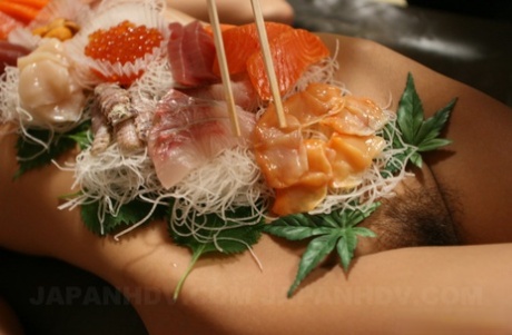 Lieve Aziatische babe Ramu Nagatsuki wordt betast terwijl ze bedekt is met sushi op een tafel