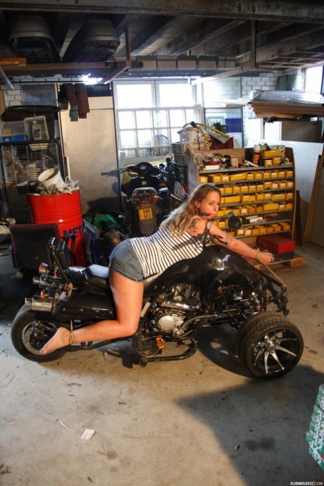 Ragazza amatoriale sottomessa che posa legata e imbavagliata su una moto