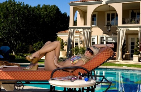 Søde blonde Jana Jordan strimler fra hendes bikini top på en solseng ved poolen