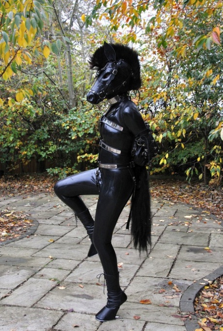Kinky slet die buiten poseert in een paardenmasker en een volledig bedekkende latex outfit
