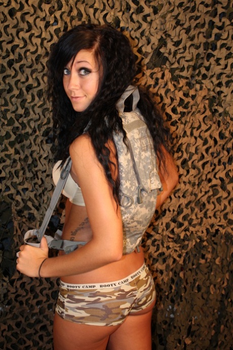 Garota de cabelos escuros, com mamas pequenas, mostra o rabo e posa com uma arma.