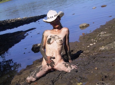 Skinny babe in a cowboy hat flaunts her tiny tits & spreads naked in the mud