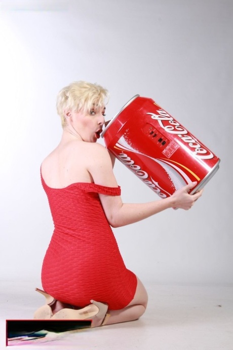 MILF aux cheveux courts dans une robe rouge sexy buvant du Coca-Cola dans une énorme canette.