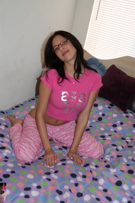 Nena amateur con gafas WouJ posando en su cama en pijama rosa