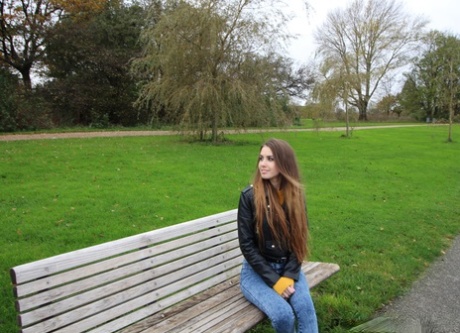 Adolescente de pelo largo con chaqueta de cuero se mete una polla dura en la boca en un parque