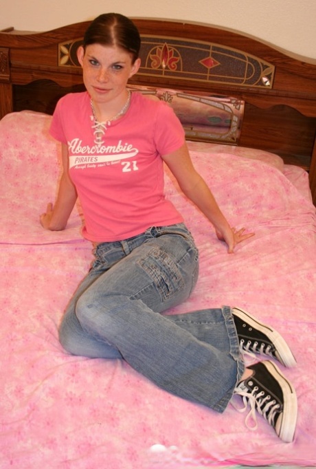 Chica amateur con pechos pequeños se desnuda y posa en una cama con zapatos