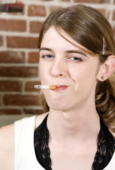 Skinny shemale Mandy Mitchell röker en cigarett och strippar på en soffa
