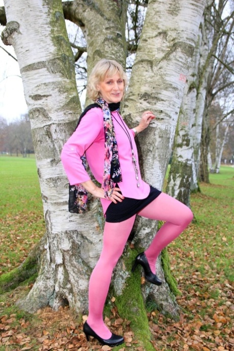 Dani, blonde et mûre, pose en tenue rose et talons dans un parc.